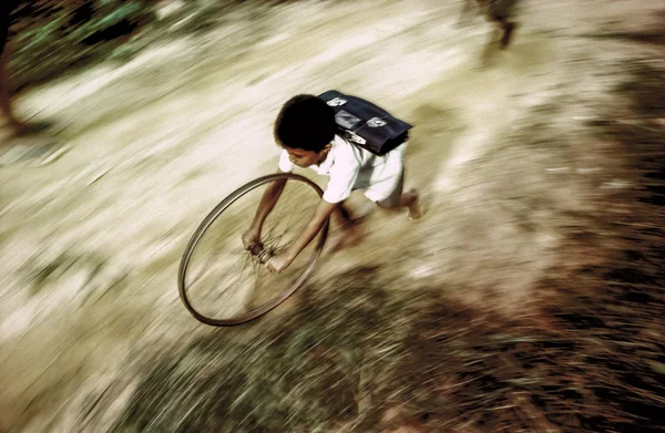 Chico en uniforme escolar corre de vuelta a casa jugando con una rueda de un b —  Fotos de Stock