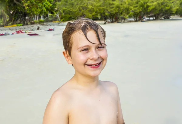 Pojken med brun blött hår är leende och njuter av stranden — Stockfoto