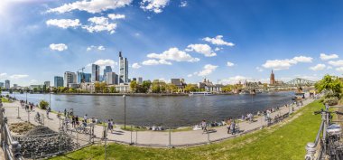 People walk along the river Main with Frankfurt Skyline