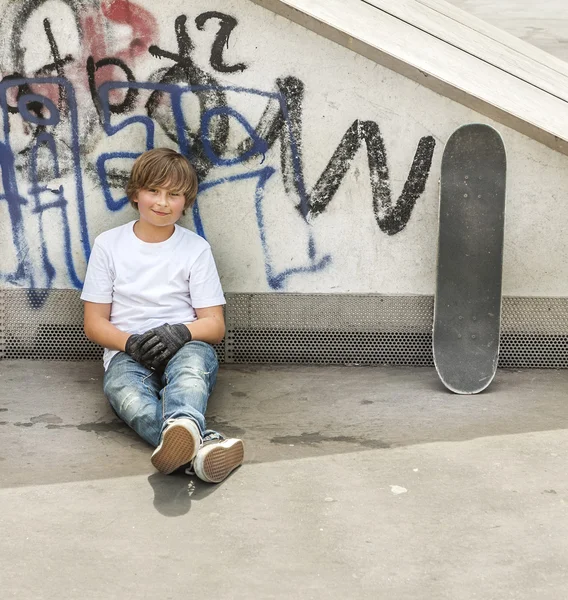 Niño se relaja con su tabla de skate en el parque de skate —  Fotos de Stock