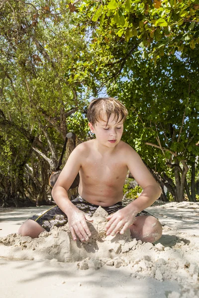 Glad ung pojke är att gräva i sanden på stranden — Stockfoto