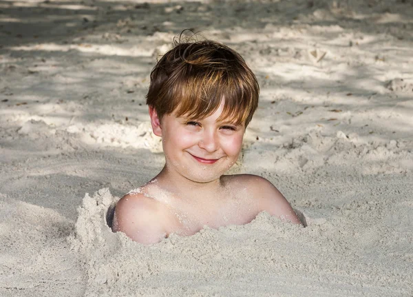 Ung pojke omfattas av fin sand på stranden — Stockfoto