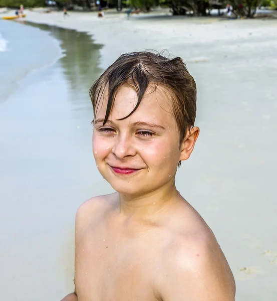 Jong gelukkig jongen met bruin nat haar is glimlachen en genieten van het mooie strand — Stockfoto