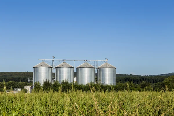 Quatro silos de prata no campo sob o céu azul — Fotografia de Stock