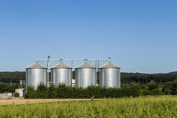 Quatro silos de prata no campo sob o céu azul — Fotografia de Stock