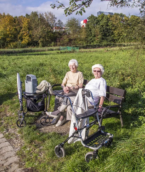 Two elderly ladies enjoy the sun at a bench and got there with a — Stock Photo, Image