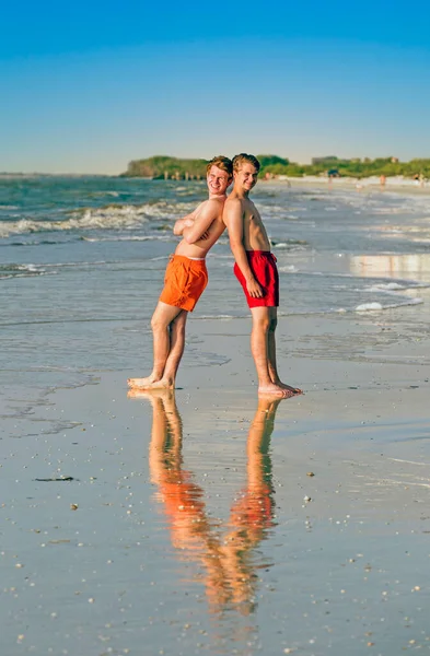 青少年们在海滩上背靠背地享受日落 — 图库照片