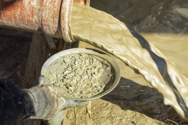 Yapay bir sondaj makinesinin çamuru ile karıştırılmış su ve bir çamaşır tavasıyla elle kontrol edilen taşlar.