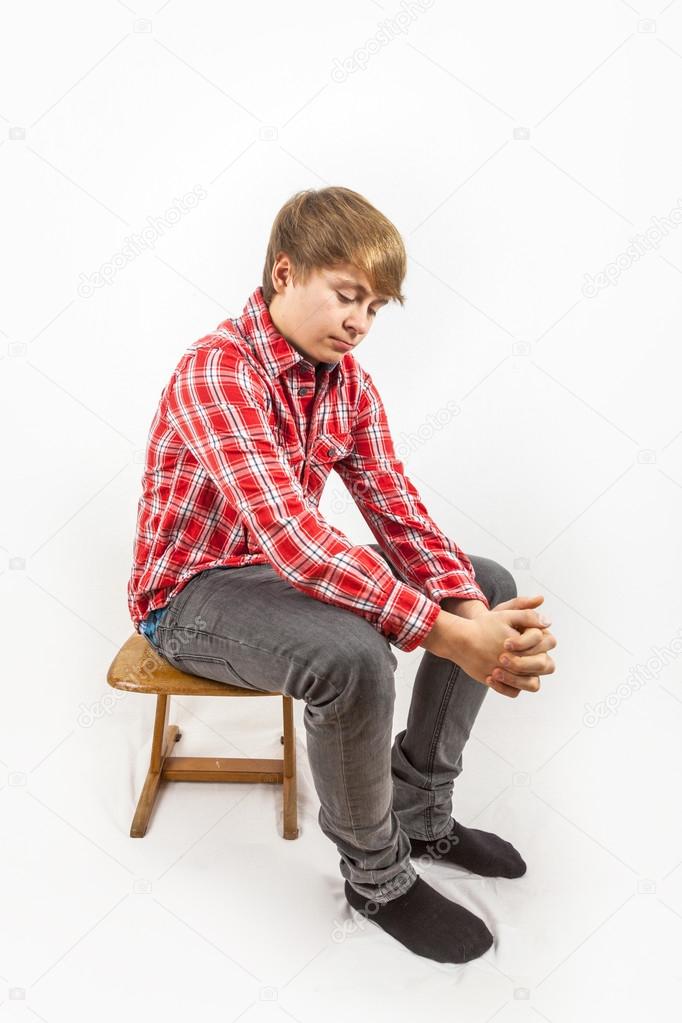 sad looking young boy with red shirt sitting on a wooden school 