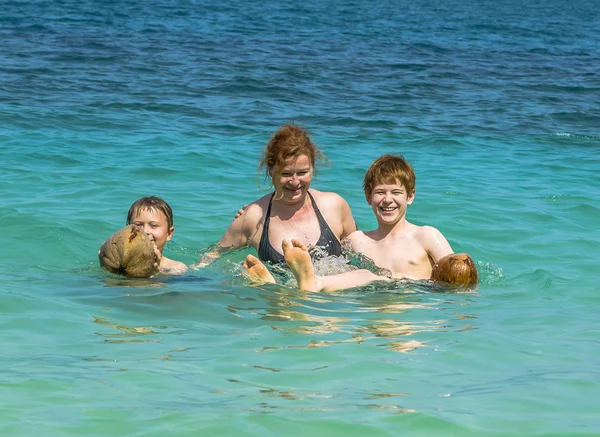 Familj spelar med en kokosnöt i havet på en vacker strand — Stockfoto