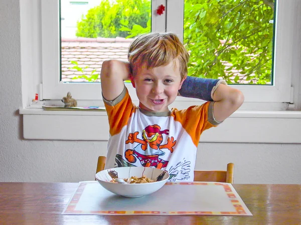 Niño con brazo en yeso desayuna en la mesa —  Fotos de Stock