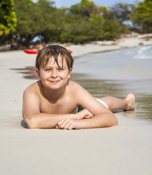 Menino se encontra na praia de areia e goza da areia quente fina — Fotografia de Stock