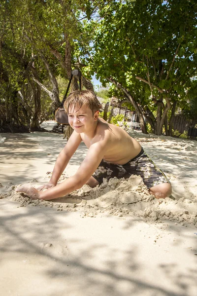 Felice giovane ragazzo sta scavando nella sabbia — Foto Stock