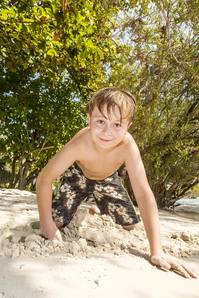 Gelukkige jongen is graven in het zand van het strand — Stockfoto