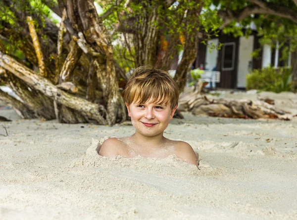 Menino feliz coberto por areia fina — Fotografia de Stock
