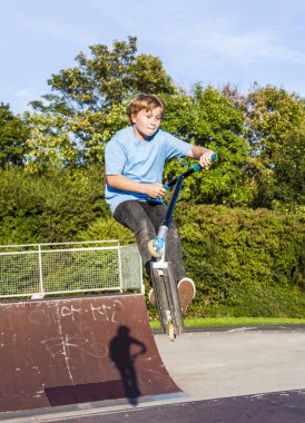 Çocuk scooter skate Park ile bir rampa atlar.