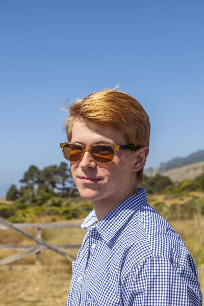 Крутой подросток в солнечных очках ходит счастливым по лугу — стоковое фото