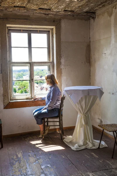 Mulher sentada à janela de uma casa velha — Fotografia de Stock