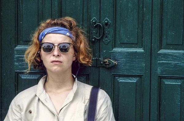 Cool looking young woman poses in front of a wooden door — Stock Photo, Image