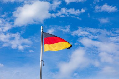 Mavi gökyüzünün altında dalgalanan Alman bayrağı