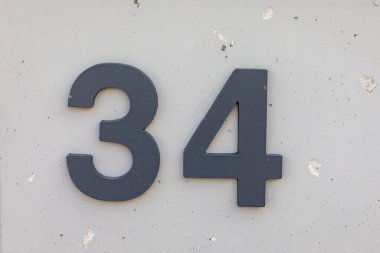 Siyah Housenumber 34 evin gri beton duvarında.