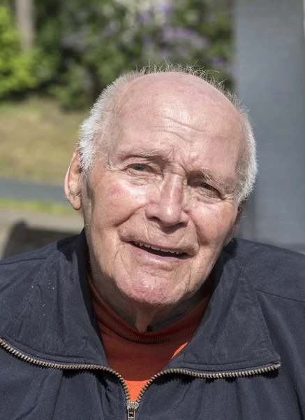 Smiling happy senior man sitting in his garden — Stock Photo, Image