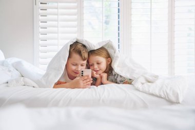 Kardeşler, mutlu ve yatakta akıllı telefonlu çocukların portresi. Evde mutlu, sevgi dolu ve eğlenceli. Aile, çocukluk.