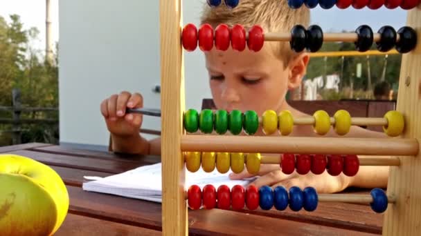 Маленький хлопчик робить домашнє завдання надворі на терасі — стокове відео