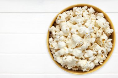 Beyaz ahşap üst görünümü üzerinde sarı kase patlamış mısır