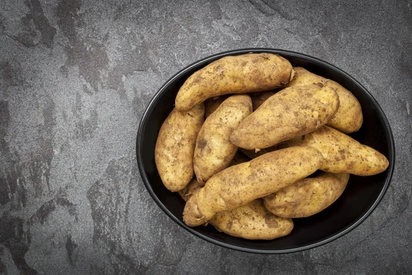 Άπλυτα ακατέργαστη Fingerling πατάτες σε μαύρο πιάτο πάνω από σκούρο πλακών O — Φωτογραφία Αρχείου