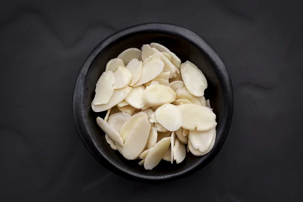 Flocos de amêndoa em Black Bowl sobre Dark Slate Overhead View . — Fotografia de Stock