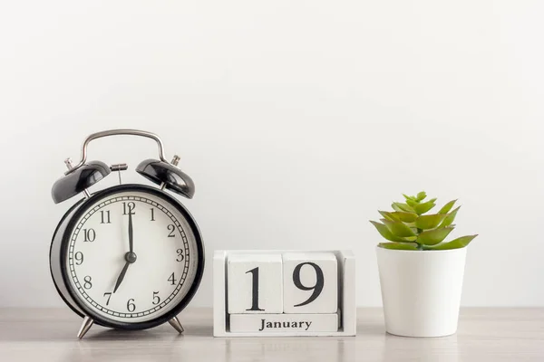 19 Ιανουαρίου σε ένα ξύλινο ημερολόγιο, δίπλα σε ένα ρετρό ξυπνητήρι και ένα ζουμερό σε μια μικρή κατσαρόλα σε ένα ελαφρύ τραπέζι.Μια μέρα τον Ιανουάριο. Χειμερινή ημέρα.Ένα αντίγραφο του χώρου.Χώρος εργασίας. — Φωτογραφία Αρχείου