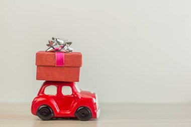 A red retro toy car delivers a gift box for a holiday on a light background.