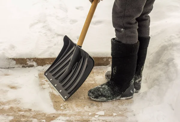 Человек в войлочных сапогах с лопатой в руках убирает снег с тротуара после снегопада.. — стоковое фото