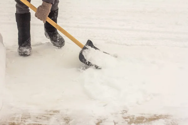 Mężczyzna w filcowych butach, z łopatą w rękach, usuwa śnieg z chodnika po opadach śniegu.. — Zdjęcie stockowe