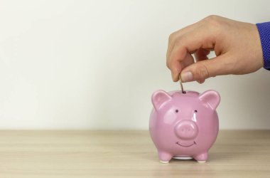 Genç adam domuz kumbarasına para koyar. Biriktirme ve tasarruf etme konsepti.