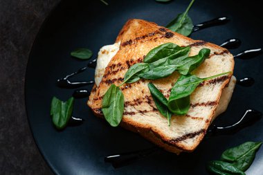 Sağlıklı tam tahıllı sandviç, taze ıspanak yapraklı çıtır tost, avokado, sahanda yumurta ve baharatlı sos. Yemek arka planda. Fikir, hızlı kahvaltı veya öğle yemeği tarifi