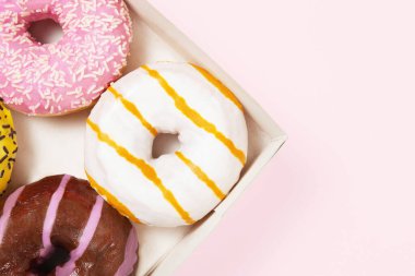 Yuvarlak renkli çörekler, üzerine serpiştirilmiş şekerler. Jöleli çörek kutusu. Pastel pembe arka plan. Farklı aromalı çörekler - karamel, çikolata, sakız.
