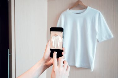 Kadın akıllı telefondan ikinci el kıyafetlerin fotoğrafını çekiyor.