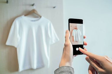 Man takes photo on smartphone of used clothing for resale clipart