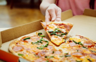 Pizza çemberinden pizza dilimi tutan kadın. Pizza kutusundan lezzetli peynirli pizza alan bir kadın. Peynir ve yeşil biber
