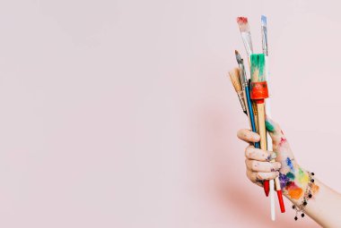 Yaratıcı bir geçmiş. Renkli boya fırçaları tutan kadın sanatçı. Arkaplanda boya ve fırça izleri var. Sanat sınıfı, sanat okulu. Pembe sanatsal arka plan, kopyalama alanı. Kirli fırçalar.