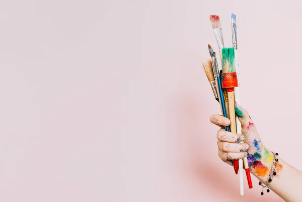 Yaratıcı bir geçmiş. Renkli boya fırçaları tutan kadın sanatçı. Arkaplanda boya ve fırça izleri var. Sanat sınıfı, sanat okulu. Pembe sanatsal arka plan, kopyalama alanı. Kirli fırçalar.
