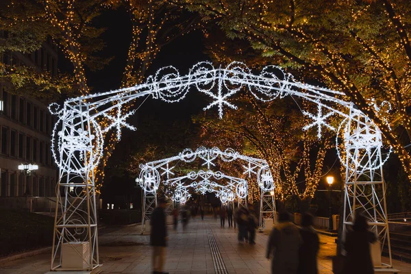 Beyaz ışıklandırılmış kemer ve ağaçların altında yürüyen yayalar akşamları, tatil mevsiminde, kentsel Noel aydınlatmasıyla süslenmiş ağaçlar.