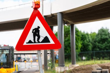 Şehir yolundaki bakım sırasında işçilerin silueti yüksek yapının yanında duran üçgen kırmızı tabela, kentsel bakım