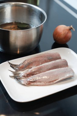 El, çiğ ringa filetosunu iyileştirmek için aromatik salamura tuz ekler, metal tencere ve temiz soba, ev yemeği, turşu balığı tarifi yanında gösterilir.