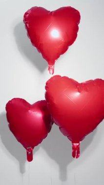 Kırmızı folyo kalp balonları dikey bir kompozisyonda yükselirler ve neşeli ve romantik bir Aziz Sevgililer Günü arkaplanı oluştururlar.