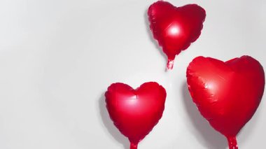 Üç parlak kırmızı folyo kalp balonu zıplar ve hafifçe yükselir, neşeli stüdyo ağır çekimde sallanır ve yükselir, Sevgililer Günü, romantik fon