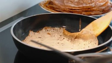 İnce krep, ahşap spatula kullanılarak sıcak tavada ters çevrilir. Krep kızarırken, buhar ve ısı görülebilir.