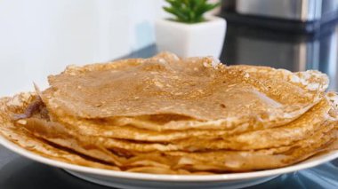 Beyaz tabak üzerine istiflenmiş sıcak ince krepler kızartmadan sonra buhar salar. Krep ve krep yığını yemeye hazır altın kahverengi yüzeyler.